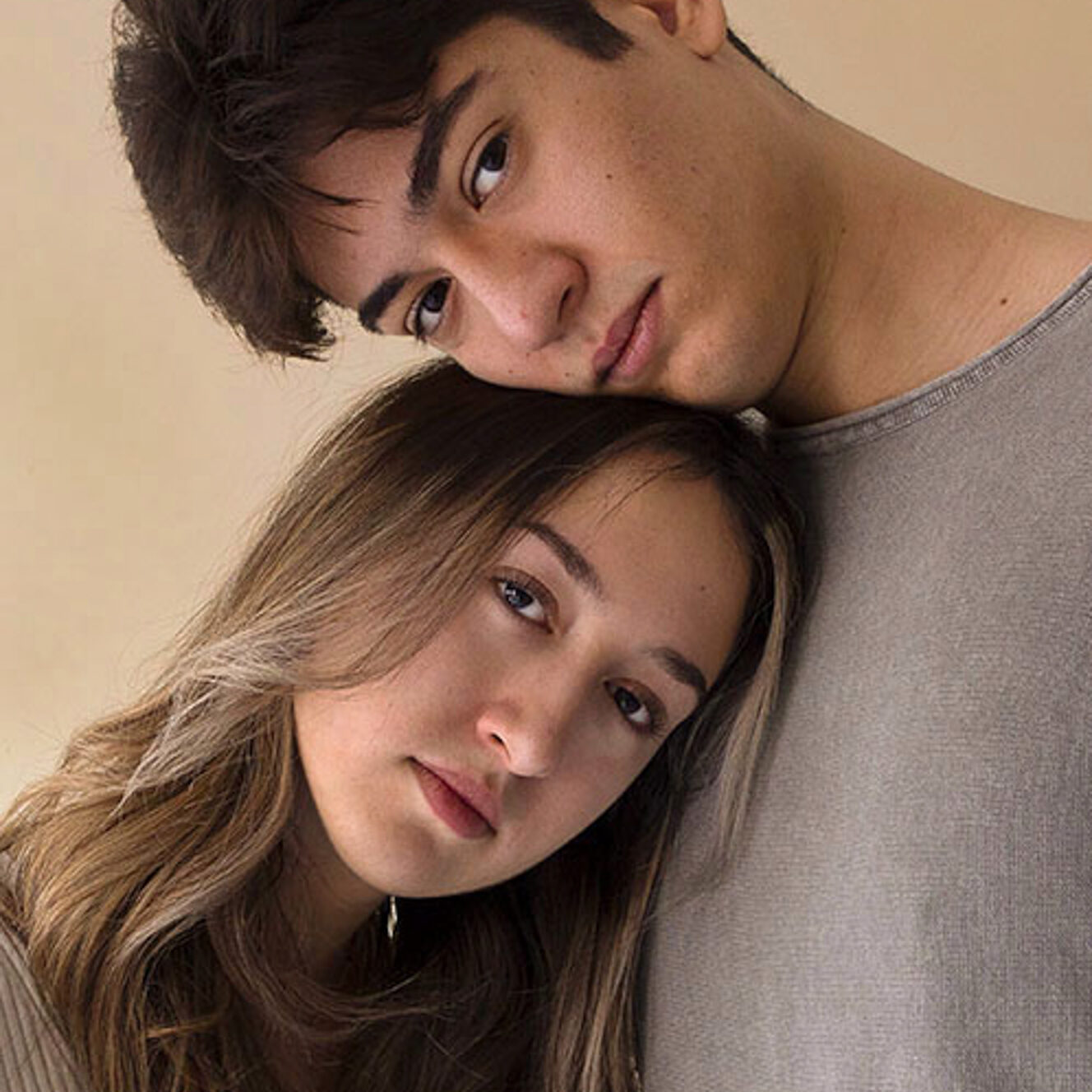 This photo consists of a self-portrait of a woman and a man. The two are wearing a beige and gray t-shirt. The woman’s head is resting on the man’s chest and his head on top of hers.