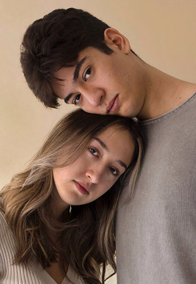 This photo consists of a self-portrait of a woman and a man. The two are wearing a beige and gray t-shirt. The woman’s head is resting on the man’s chest and his head on top of hers.