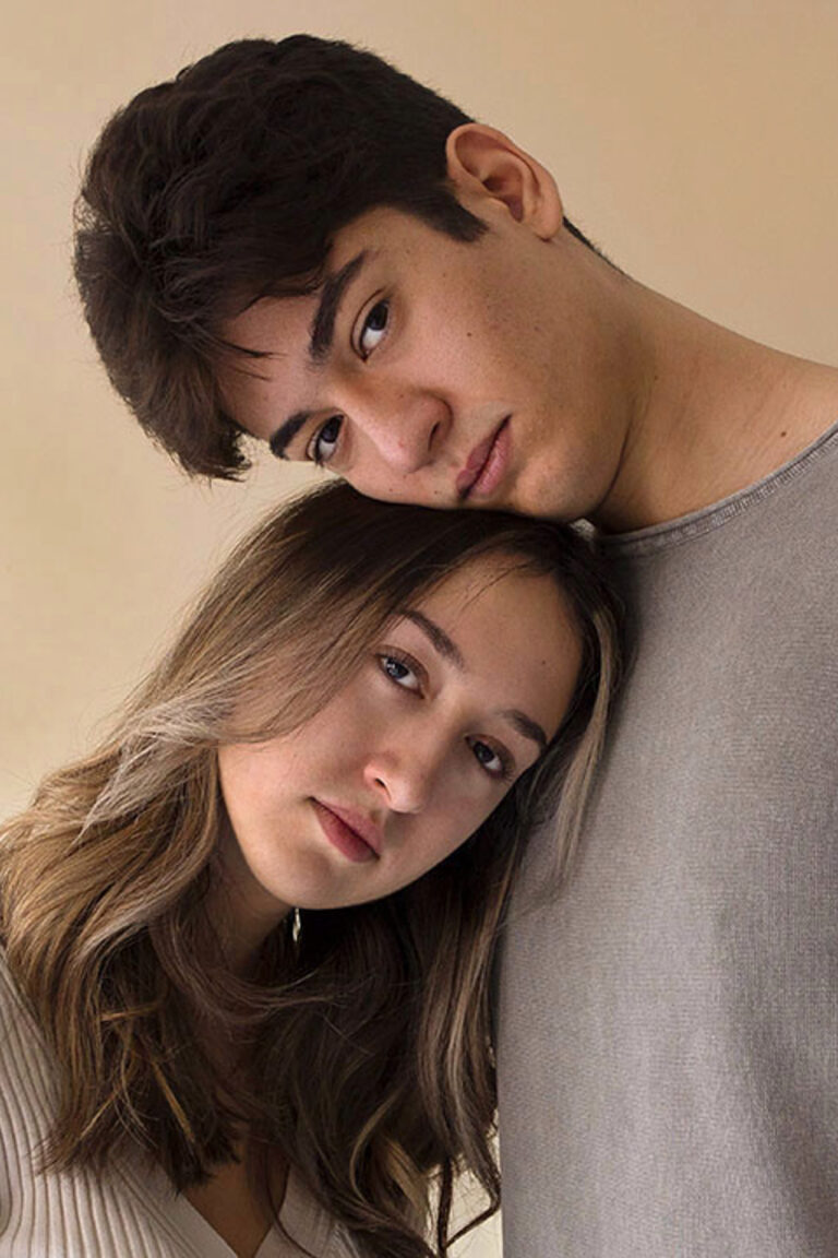 This photo consists of a self-portrait of a woman and a man. The two are wearing a beige and gray t-shirt. The woman’s head is resting on the man’s chest and his head on top of hers.