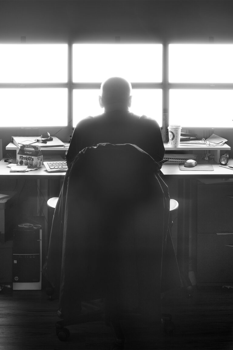 A security attendant sits at a desk awash in the light from an array of six monitors.