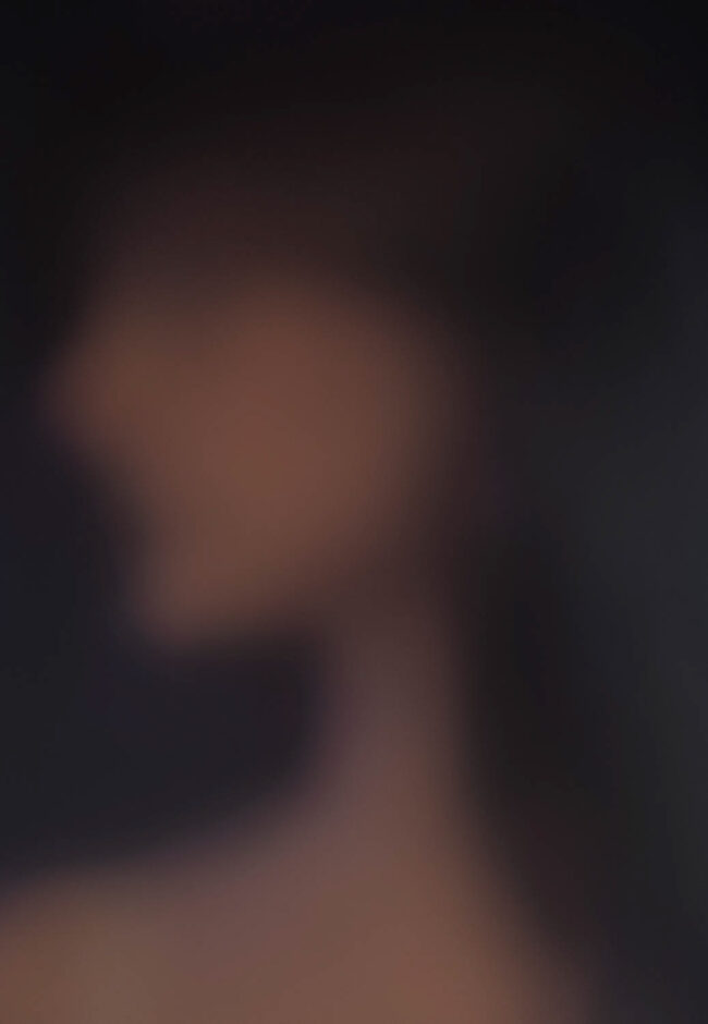This photograph shows a blurred side profile of a person. The colours of beige purple and black are blurred throughout the photo and only a faint silhouette is able to be made out.
