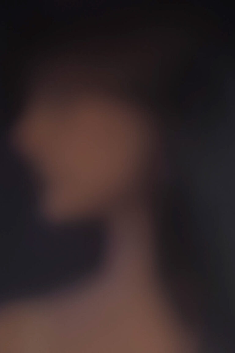 This photograph shows a blurred side profile of a person. The colours of beige purple and black are blurred throughout the photo and only a faint silhouette is able to be made out.