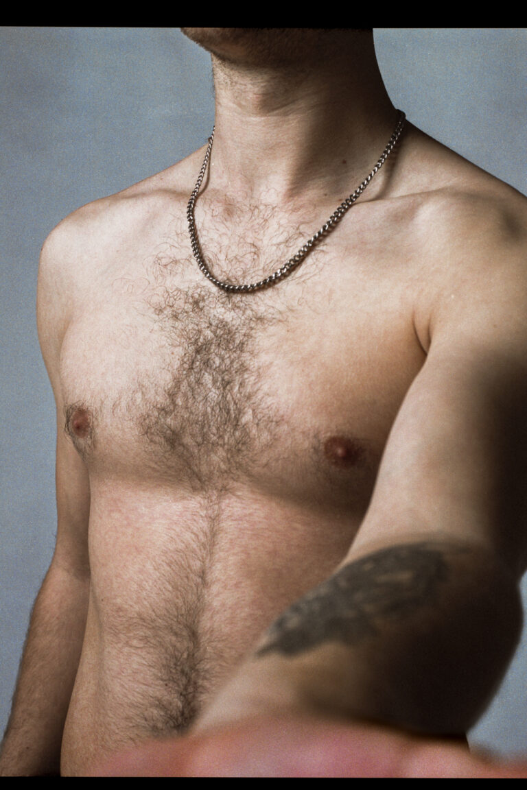 The image depicts a shirtless caucasian man with tattoos, grasping out to the camera as the figure (face not shown) confronts the lens.