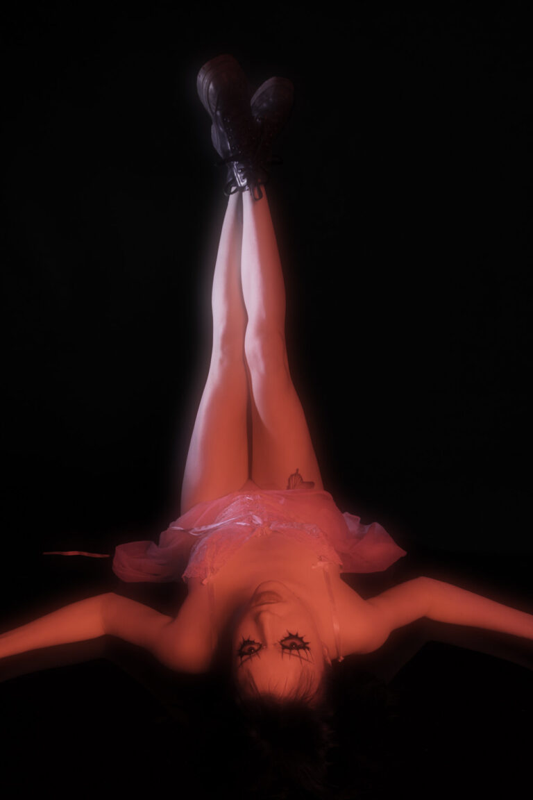 Metal Human portrait of a person with black hair laying upside down with their feet in the air wearing a lace dress and black shoes, the person is lit entirely with red lighting