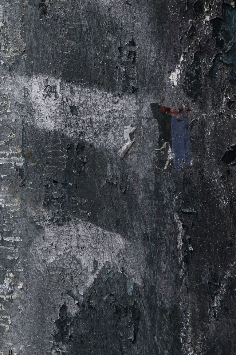 This is a zoomed in photo of a dark green telephone pole. On the right side of the photo there is a sticker on the pole that is plain white, it appears as if the sticker that was once there has been peeled off leaving the white adhesive part of the sticker. The pole appears to be peeling, there are red and white markings covering the pole. On the right side of the photo, the pole has horizontal straight lines going down it where the material the pole is made of is peeling which created alot of white patches.