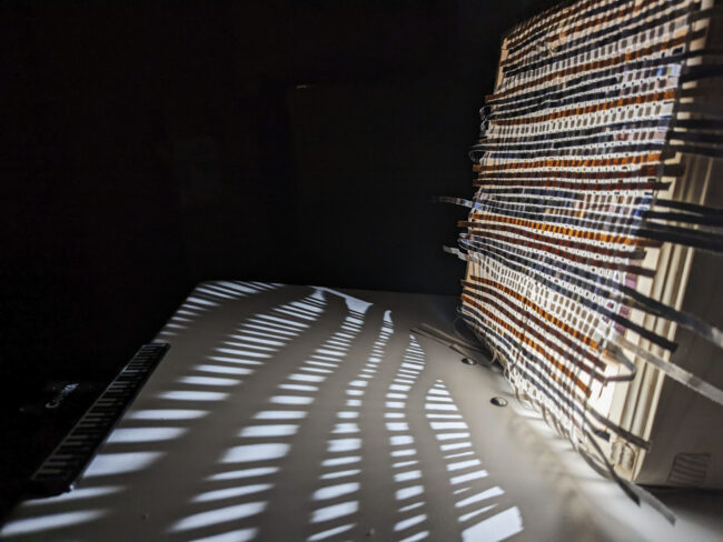 This image is a close up of what happens when a rather weak source of light is projected through the mesh created by weaving strips of recycled paper.