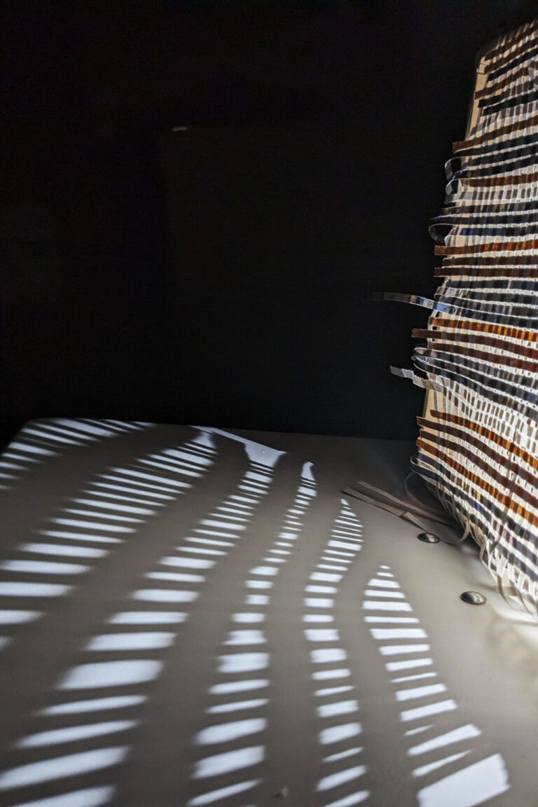 This image is a close up of what happens when a rather weak source of light is projected through the mesh created by weaving strips of recycled paper.